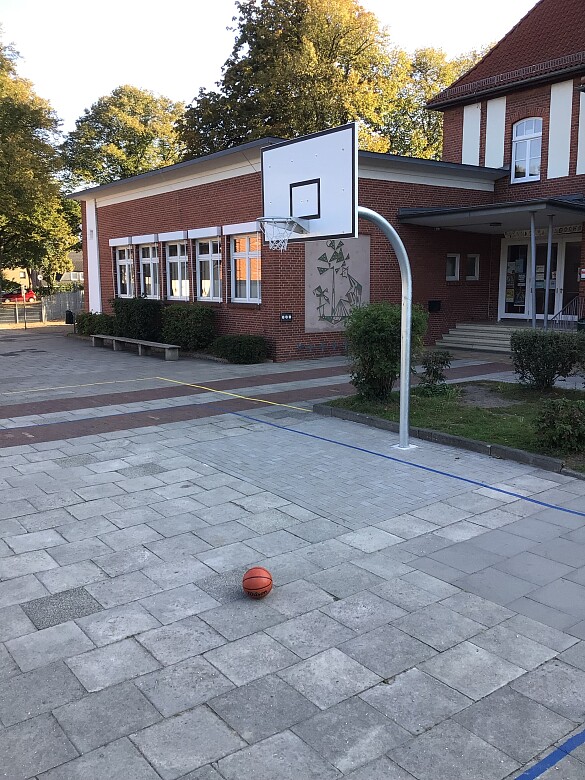 auf dem Foto ist ein Basketballkorb und ein Basketball zu sehen, im Hintergrund das Gebäude der Schule Arbergen