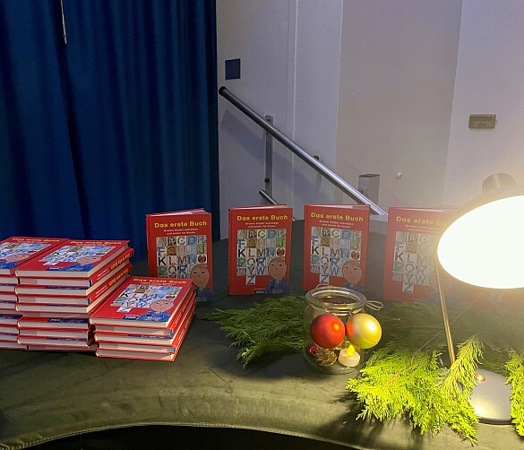 Zahlreiche Exemplare des ersten Buchs liegen auf dem Klavier in der Aula. Das Klavier ist mit einer grünen Decke, Tannenzweigen und Adventsschmuck dekoriert.