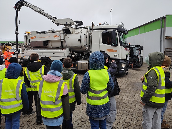 Kinder in Warnwesten stehen vor einem Fahrzeug der Bremer Straßenreinigung.